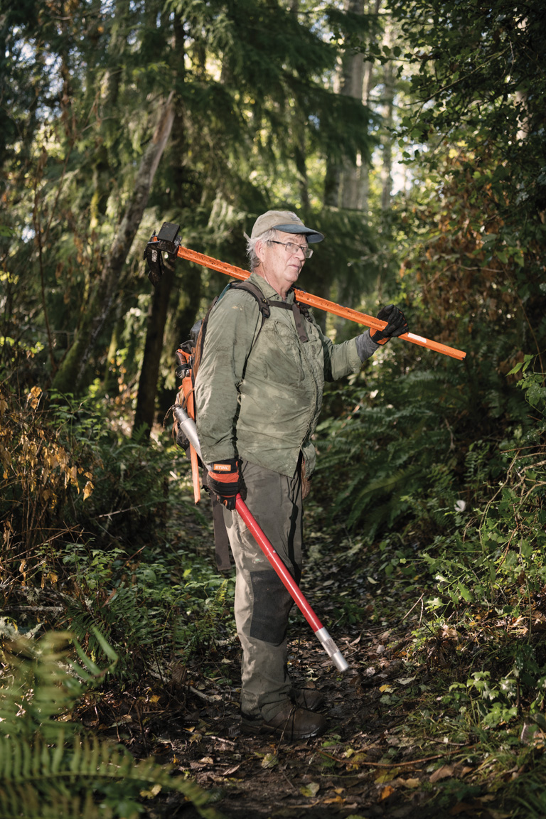 Henry Mustin holds an orange weed wrench and a red EZ-Ject lance for controlling holly on Vashon Island, Washington.