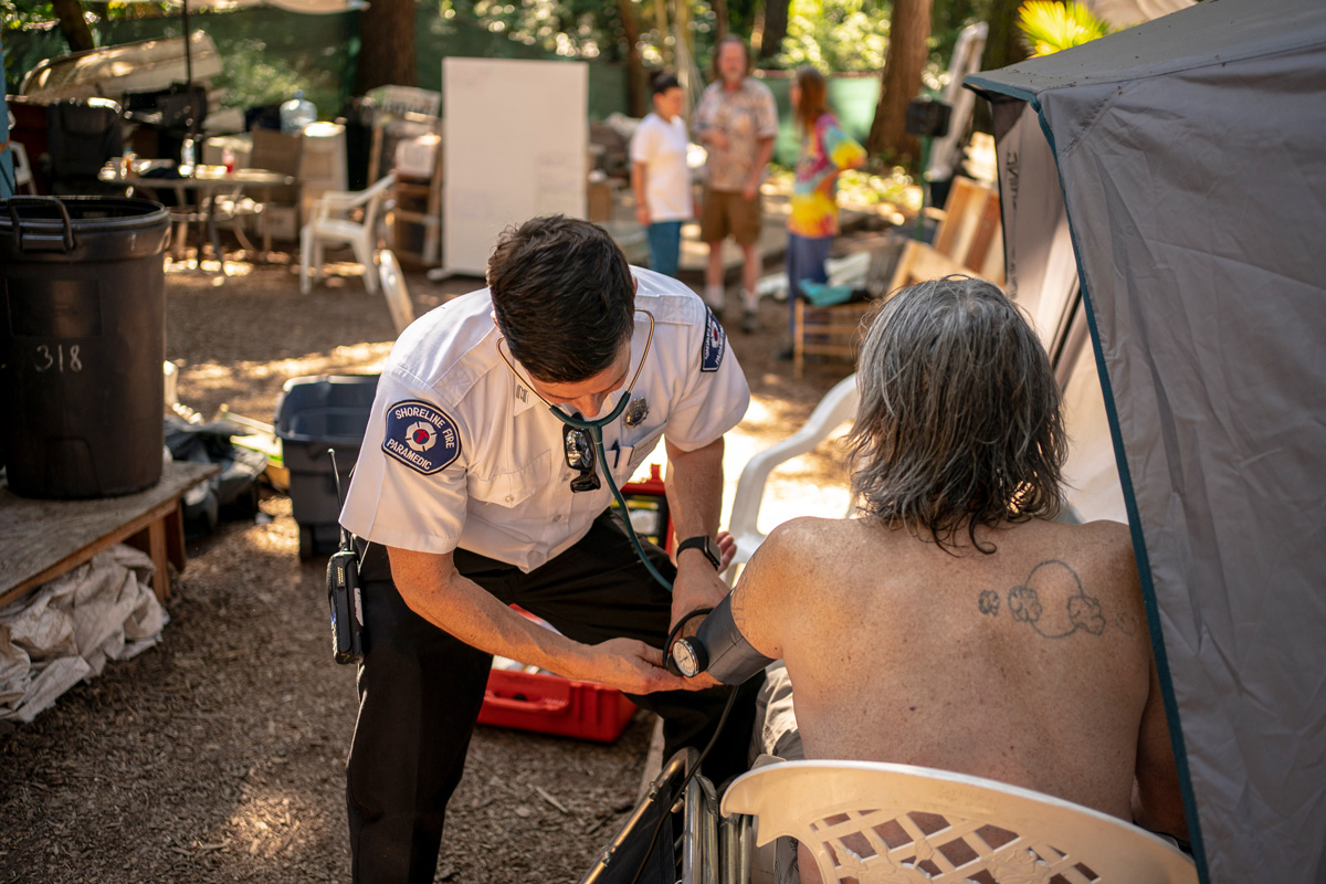 During a heat wave last July, Gabe DeBay, medical services officer with the Shoreline Fire Department, checks the blood pressure of an unhoused man at a tent encampment in Shoreline, Washington. Heat in the Pacific Northwest is already higher than normal this year. Unhoused people and outdoor workers are among those at highest risk in more moderate, early heat.