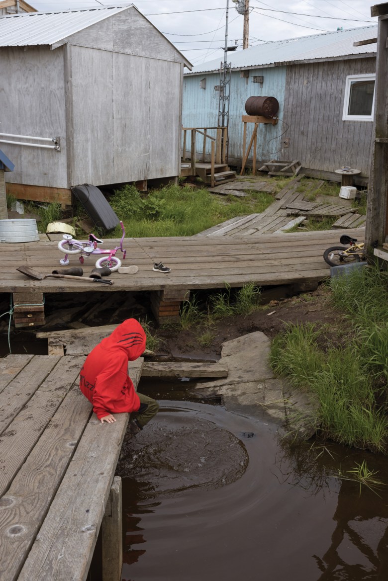 Kenton Isaac, 5, one of Susanna Isaac’s grandchildren, splashes his feet in the water near his home in Akiuk, the older side of Kasigluk. “Come spring, the water goes all the way under the sidewalks we walk on,” Susanna Isaac said this summer.  The spring floodwaters still had not receded by mid-July.
