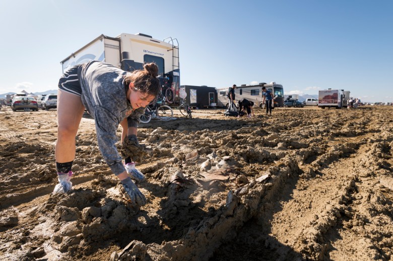 Burning Man attendees pick up litter amid the mud ruts caused by vehicles driving after rain at the festival in northwestern Nevada’s Black Rock Desert.