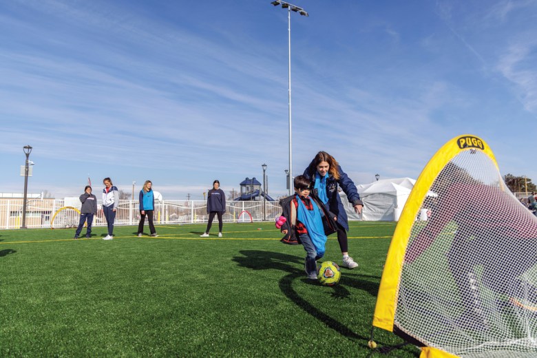 A young athlete joins MSU Denver women’s soccer players on the cover park field..