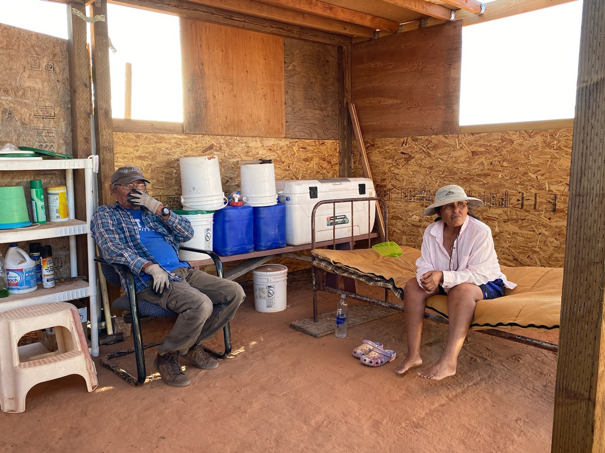 Tara Benally’s parents sit in their chaha’oh. They use buckets and barrels to haul water to their garden almost every day.